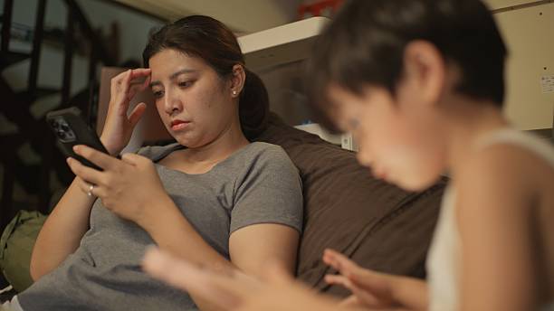 istock Asian mother working on laptop on sofa while her son watches tablet after coming home from school. 2248525013