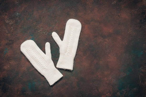 White fluffy knitted mittens on dark grunge background, top view, flat lay