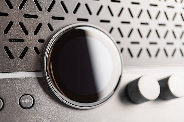 Modern gray mini guitar amp speaker, close-up view of an electronic device Focus on illuminated power button power with reflective circular elements, surrounding circles or vents possibly for heat