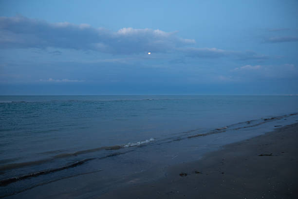 Moon in the clouds over the sea before dawn, night seascape