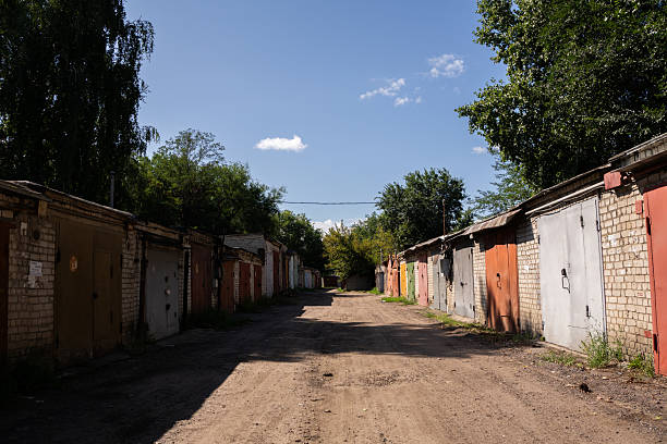 A long row of old garages with colorful metal doors lines a dirt road under a bright blue sky.