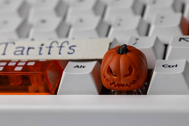 istock scary jack-o'-lantern keycap sits on a clean mechanical keyboard, next to an orange shift key and a paper tag with the word 'tariffs,' symbolizing trade issues 2248534838