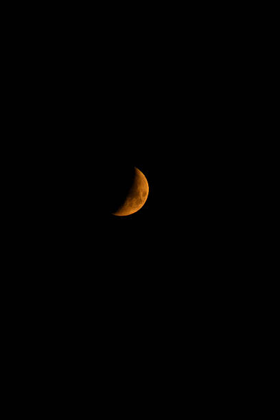 A bright orange crescent moon hangs in the dark night sky creating a minimal celestial scene.