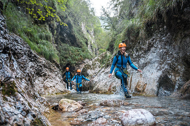 Equipped with neoprene suits and safety helmets, diverse friends embark on an outdoor excursion, walking through water canyons during an exciting canyoning experience.