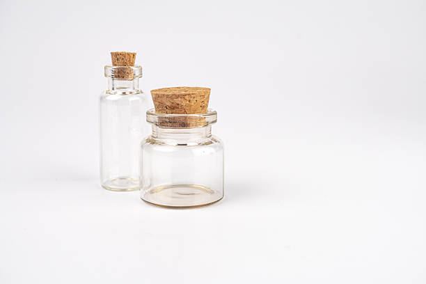 Clear glass bottles on a neutral background Three bottles, one large and two stacked smaller ones Each bottle has a cork stopper and a uniform light color Neutral gradient backdrop highlights the