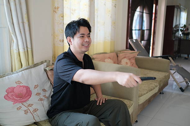 A man is sitting on a couch with a remote in his hand. He is smiling and he is enjoying himself