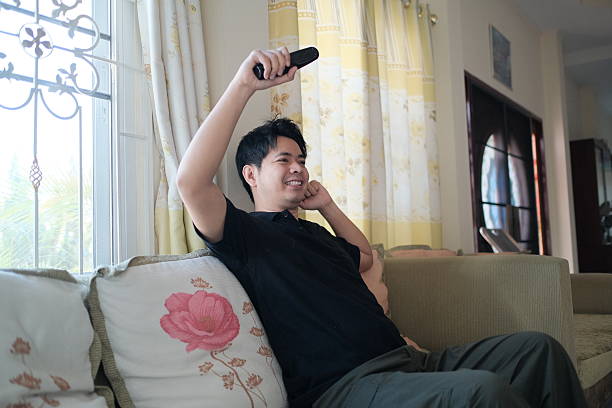 istock A man is sitting on a couch with a remote in his hand 2248539605