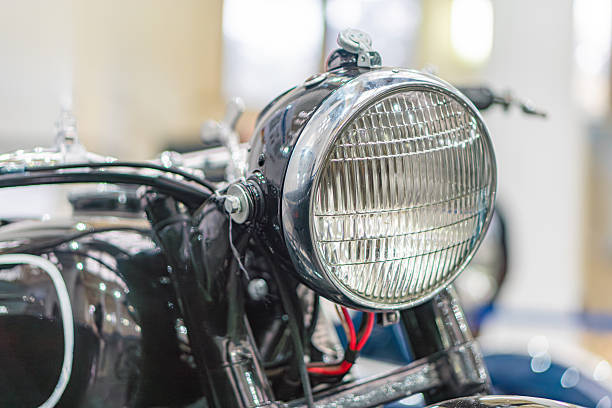 istock Vintage motorcycle on display at a car show, dark body with gleaming silver headlight, large round headlight in protective grid casing, small white label with barcode, indoor event, artificial lighti 2248541798