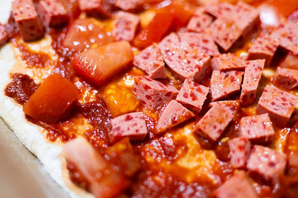 Neapolitan-style homemade pizza: sausage cubes and fresh tomatoes before baking.