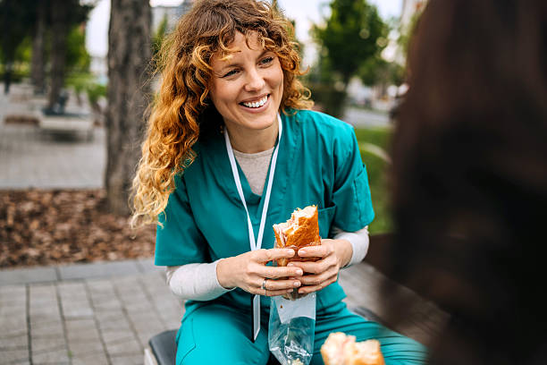 istock Two female nurses having breakfast while sitting on a bench outdoors in city 2248542755