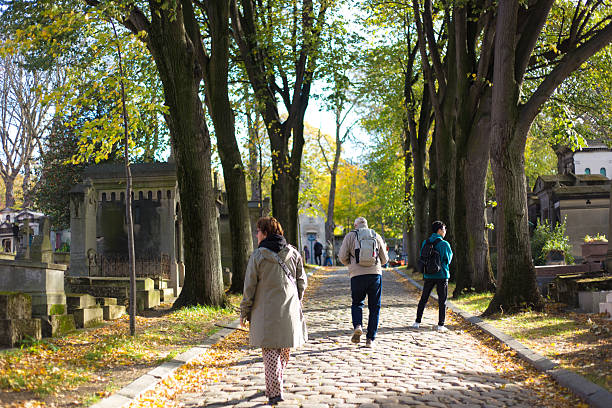 Paris, France - October 24, 2025: Visitors on a cobbled lane at Pere Lachaise Cemetery on a sunny autumnal day, 11th arrondissement.