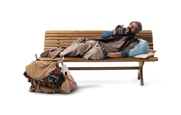 A homeless man sitting on a wooden bench, yawning before lying down, isolated on a white background, illustrating poverty, hunger, urban hardship, and survival.