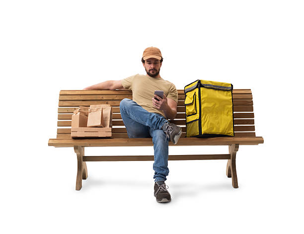 istock Food delivery man sitting on a bench using a smartphone. Isolated on white background 2248550315