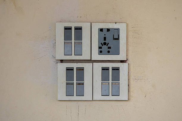 Close-up of a modern modular electrical gang switch set and power socket installed on a wall. This common electrical wiring hardware is used in residential and commercial buildings in Bangladesh.