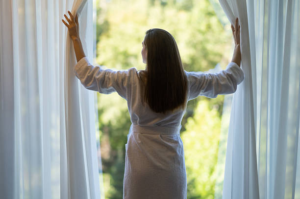 istock Long-haired woman in bathrobe opening curtains in a hotel suit 2248555501