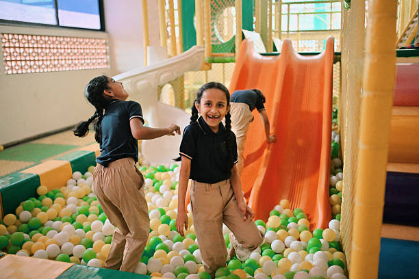 Schoolchildren enjoy a colorful indoor ball pit and slide area, laughing and playing together. Their joyful expressions reflect the importance of play and friendship during school time. Childhood happiness and playful energy in a safe and engaging environment. Early education, kids’ recreation, happiness, and playful learning environments.