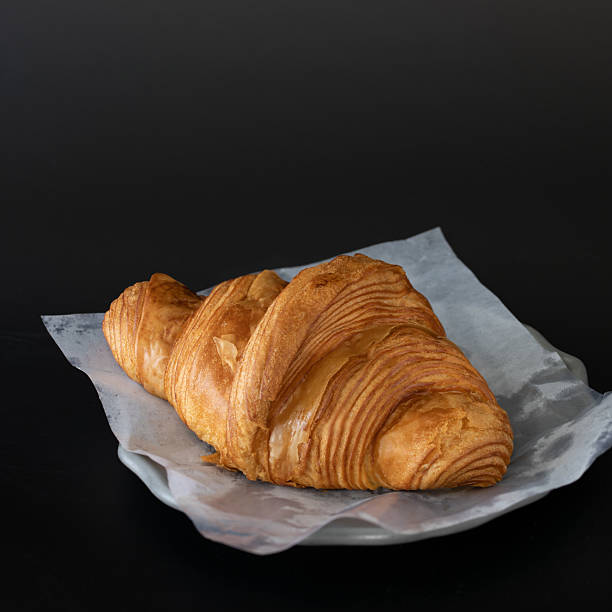 Fresh Golden Croissant on Parchment Paper Against Black Background