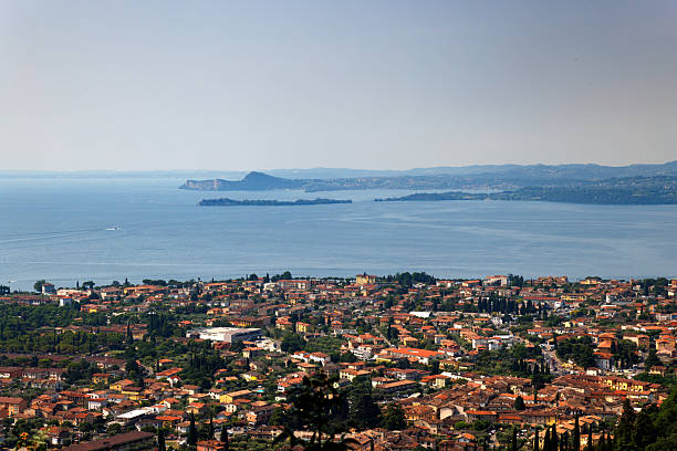 A panoramic view of Desenzano del Garda, Italy, overlooking the terracotta rooftops of the town, the prominent church of Santa Maria Maddalena, and the deep blue waters of Lake Garda.