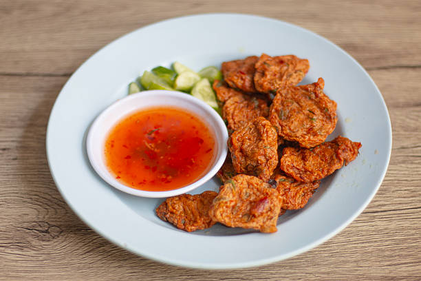 Fried fish cakes served with dipping sauce and sliced cucumber, served on a plate. Central Thai food.
