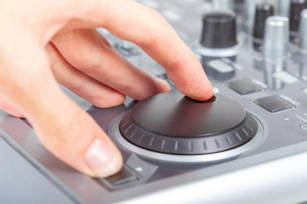 Hand using a generic jog wheel on audio video mixer console or DJ equipment finger adjusting shuttle dial for mixing and playback control professional studio equipment closeup buttons knobs one person