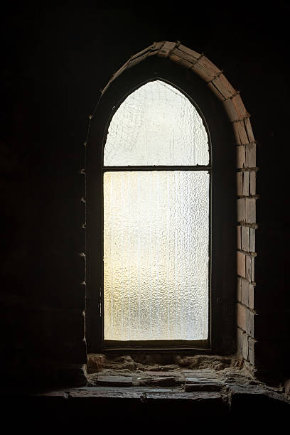 istock Arched frosted glass window in an old brick wall textured pane glowing, daylight seen from inside of a dark darkened room interior vintage gothic architecture narrow vertical opening basement attic 2248565913