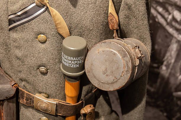 Old German soldier uniform with a stick grenade and metal gas mask storage container on a belt field gray clothes closeup detail, historical military equipment concept one person, reconstruction