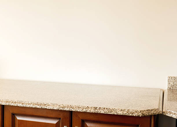 Empty granite countertop on wooden cabinets with beige white wall, clean copy space surface for product placement in kitchen or lobby room interior, polished stone worktop, daylight background, nobody