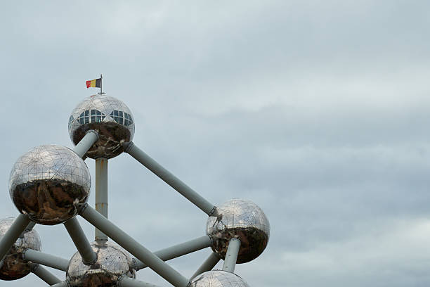 Brussels, Belgium; 18th of November, 2025. Detailed view of the Atomium's upper dome structure topped with the Belgian flag. The overcast sky enhances the reflective metallic spheres of this iconic Brussels landmark.