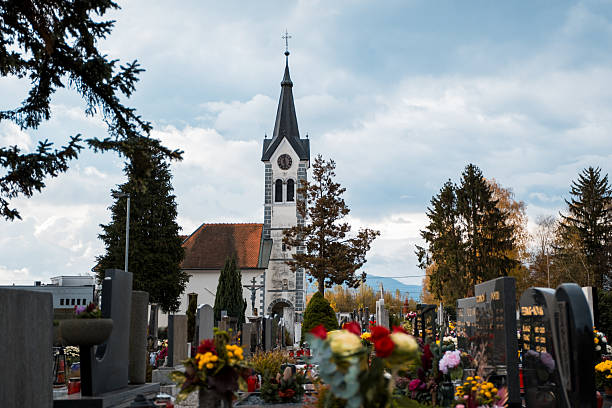 Peaceful church with clock tower surrounded by gravestones and colorful flowers in a cemetery during a calm autumn day.