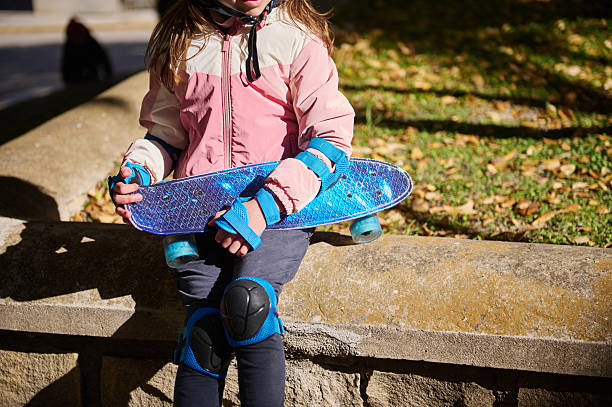 istock Kid With Blue Skateboard On Park Wall In Fall Light Wearing Pink Jacket And Knee Pads 2248572243