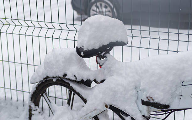 A bicycle stands outdoors with its saddle buried under a thick layer of fresh snow. The scene captures cold weather, seasonal stillness, and urban winter mood, highlighting frozen textures and quiet snowy atmosphere.