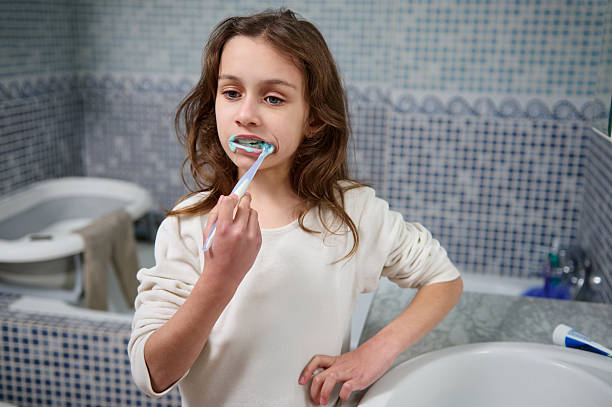 istock Young Girl Brushing Teeth in Bathroom Mirror During Morning Routine 2248572431