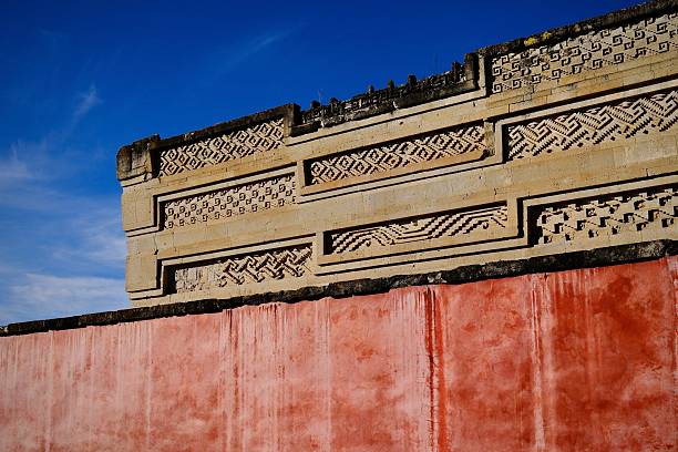 Mitla, Oaxaca, Mexico – November 11, 2025: A pink wall supports the upper carved friezes of a Mitla structure glowing in afternoon light.