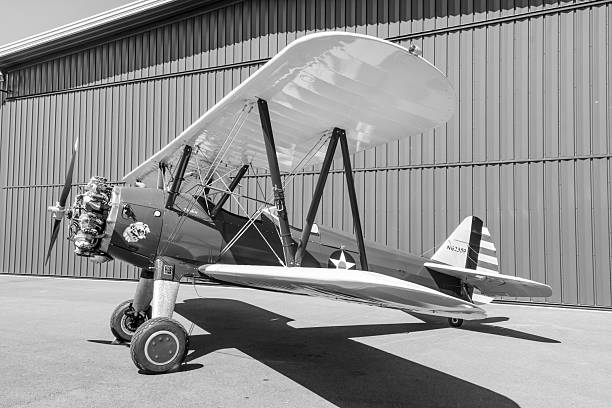This black and white vintage looking image shows a classic WWII training aircraft.  The propeller biplane is parked on the ramp in front of a hangar. These aircraft were used extensively as a primary trainer for both the US Navy and US Army Air Corps in the 1930s and 1940s.  The photo was taken in July 2025 at the Bremerton Airport, Washington, USA