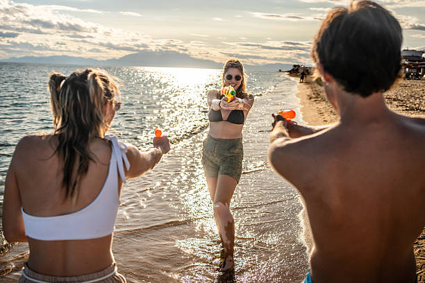istock Young friends having water gun fight at beach during sunset 2248576457