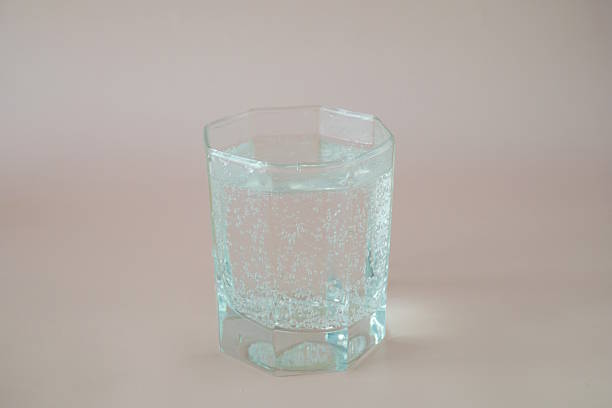 A glass of water on a pink background.