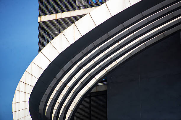 Close-up view of a modern building featuring sleek curves and lines against a blue sky, showcasing contemporary architectural design elements and textures.