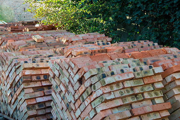 Stacked bricks rest atop a partially constructed building at a construction site, with bright sunlight illuminating the scene during the day.