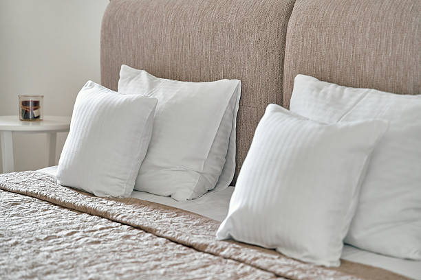 istock Elegant Bedroom Setting Featuring Plush White Cushions on a Soft Beige Headboard with a Cozy Blanket and a Decorative Candle for Relaxation 2248591217