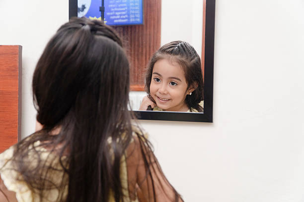 Little girl smiling at own reflection in mirror, expressing happiness and innocence