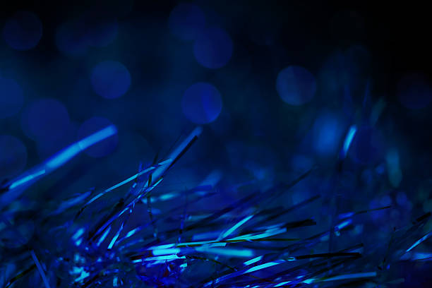 Shimmering tinsel strands close-up. The background features soft, blurred blue lights that enhance the festive atmosphere. Nice bokeh, space for copy.