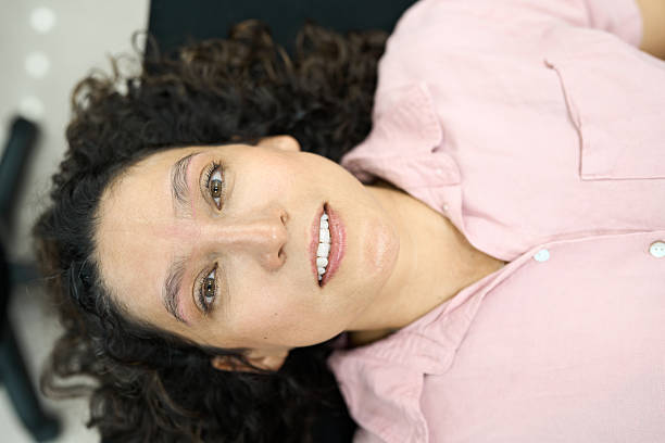 Woman lying down receiving an eyebrow microblading cosmetology treatment, smiling and looking at camera