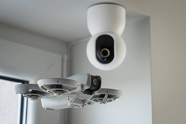 istock Modern smart home technology concept showing a small white drone hovering near a ceiling mounted security surveillance camera indoors 2248597339