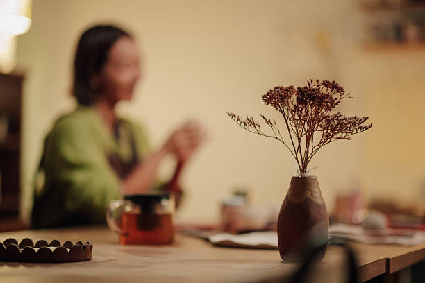 Dried flowers in a small vase creating a beautiful centerpiece on a wooden table, with a blurred woman in the background. Cozy atmosphere