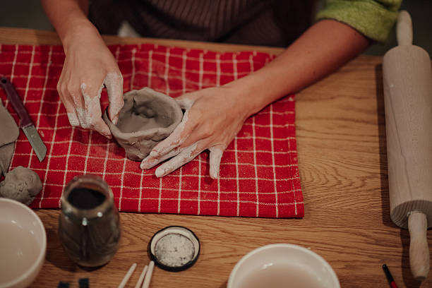 Person's hands molding wet clay into a small bowl, shaping new ceramic art during a pottery workshop