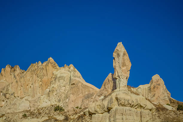Cappadocia rock formations in Turkey under clear daylight, showing tall sandstone chimneys, textured cliffs, natural erosion shapes, geological landscape, travel destination, scenic terrain, unique stone structures