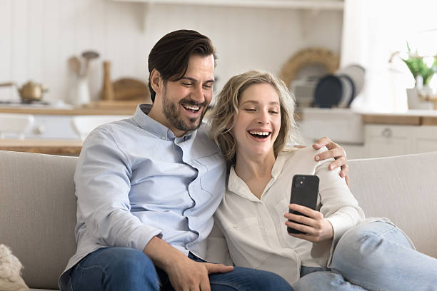 istock Overjoyed couple cuddle on couch laughing looking at phone screen 2248606957
