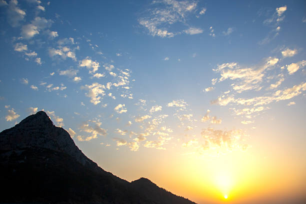 Sunset casts warm hues across the sky as it descends behind rugged mountains in Turkey. The clouds reflect soft colors, enhancing the tranquil ambiance of the natural landscape.