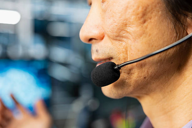 Close up of senior programmer in data center speaking in headset mic, using AI to provide user technical support. Asian man in server room assisting clients during remote call using AI