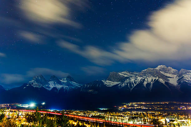 A view of the town of Canmore in Alberta, Canada, at night. The Three Sisters Mountains are visible on the left. The lights from the traffic on the Trans-Canada Highway are visible at the bottom.
